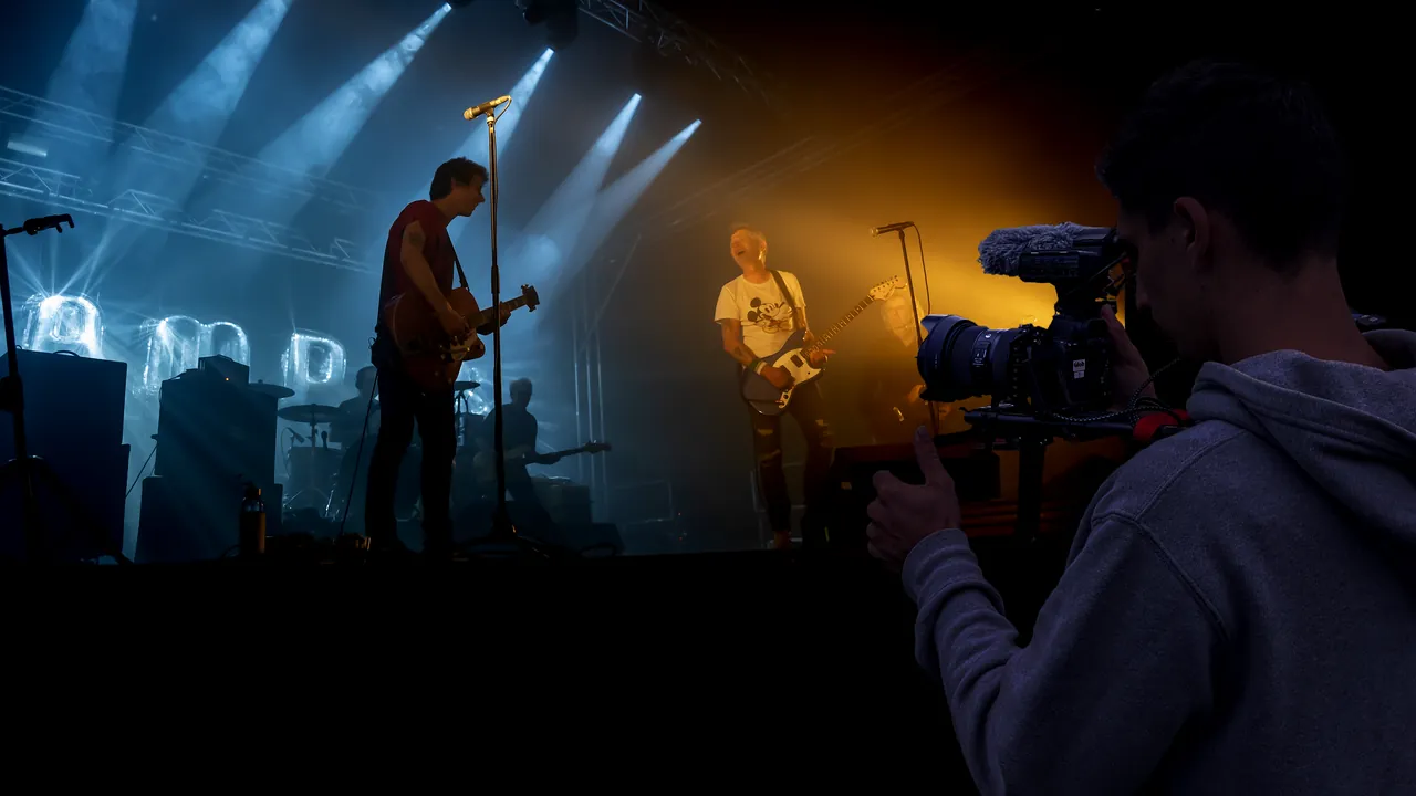 Vidéaste équipé d'une caméra et d'un micro filmant un concert depuis le bord de scène