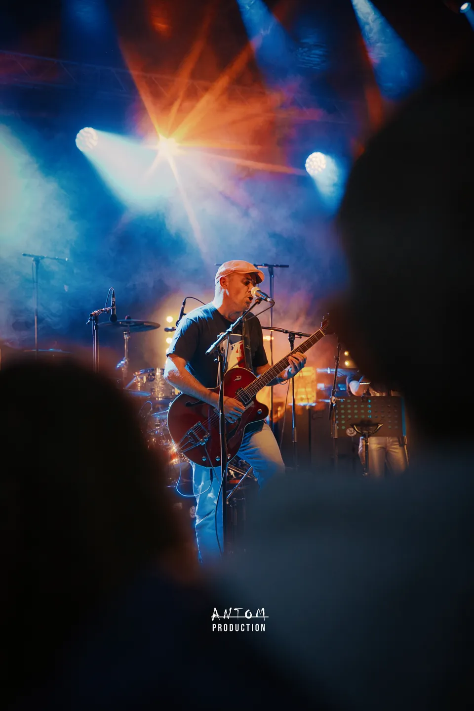 Concert vu depuis le public : guitariste éclairé par des projecteurs orange et bleus
